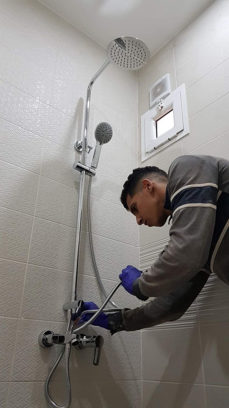 Plumber fitting a chrome rain shower riser and mixer valve in a tiled shower