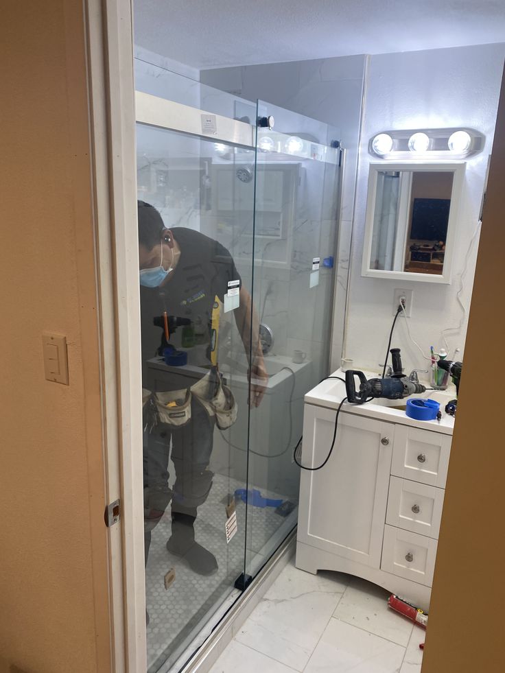 Technician working inside a new glass shower enclosure during a bathroom renovation