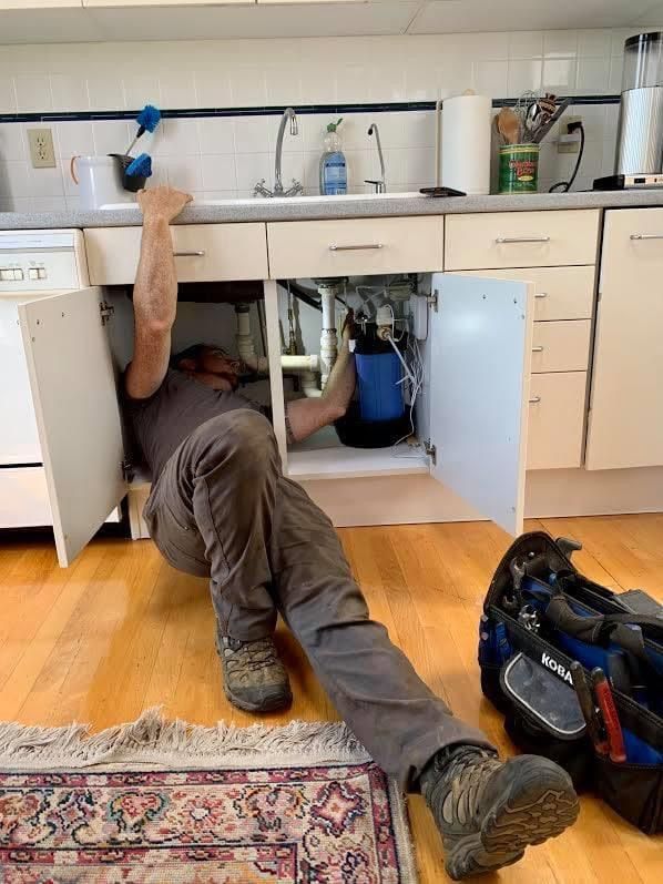 Plumber under a kitchen sink installing a water filtration unit